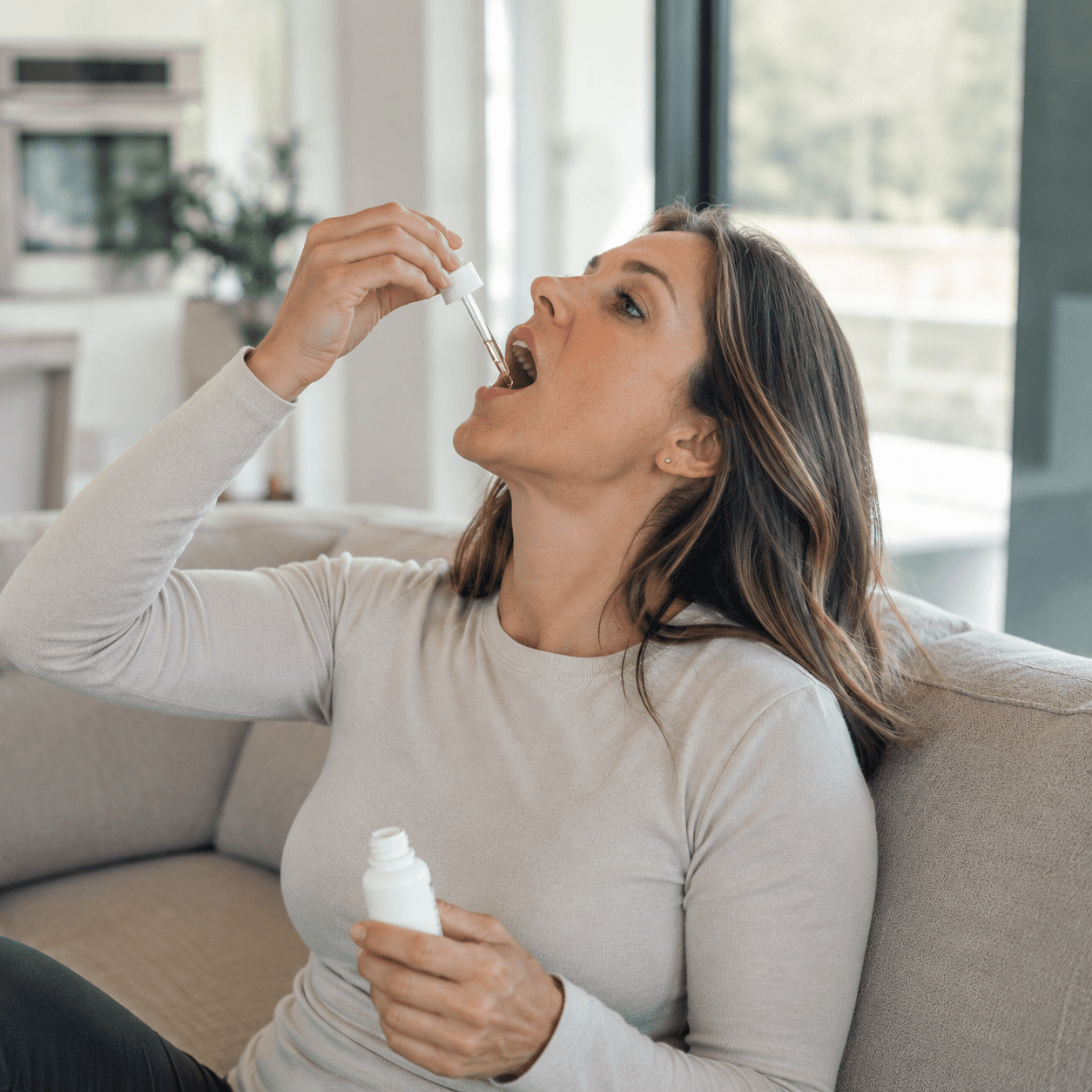 Woman placing wellness tincture drops under her tongue while relaxing at home in the evening